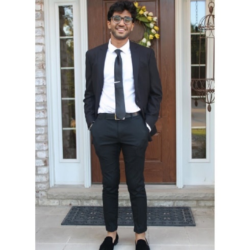 A person wearing a suit and tie standing in front of a building Description automatically generated